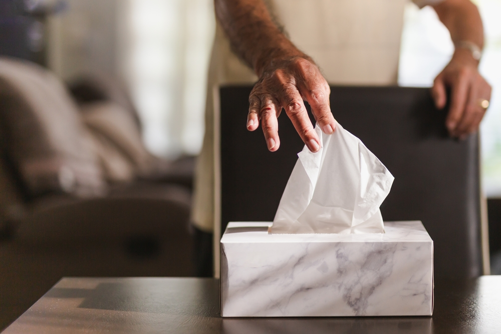 man pulling a tissue from the tissue box on a table