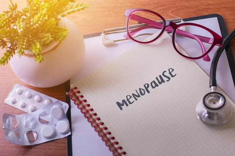menopause written on notebook with pink glasses and stethoscope, fake plant, and white pills